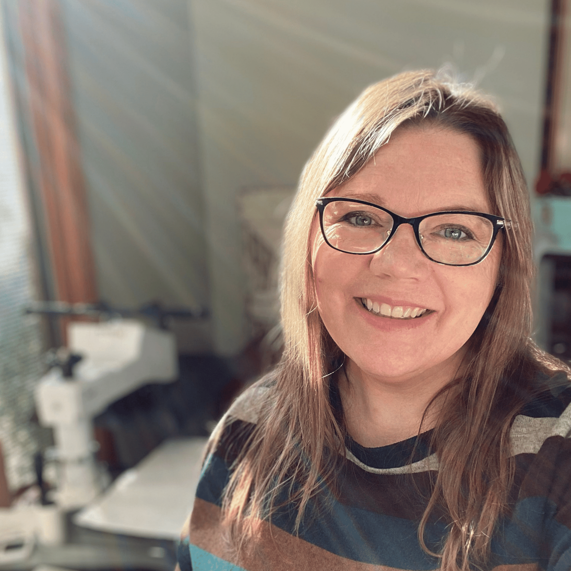 Photo of Larissa Smiling with her heat press and the beautiful barn door she uses as a backdrop for her product images in the background.