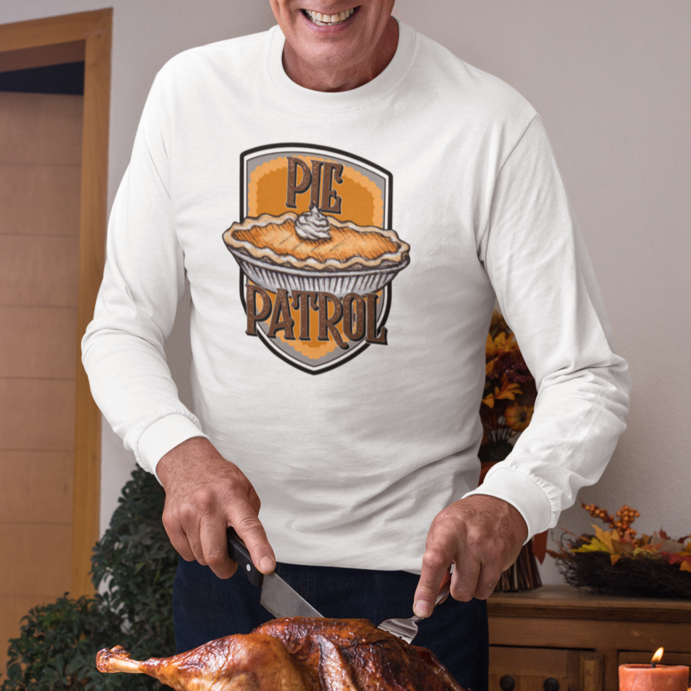 Smiling man wearing a long sleeve T-shirt with a pumpkin pie and the words "Pie Patrol" on the chest, while he's carving a turkey for Thanksgiving dinner.