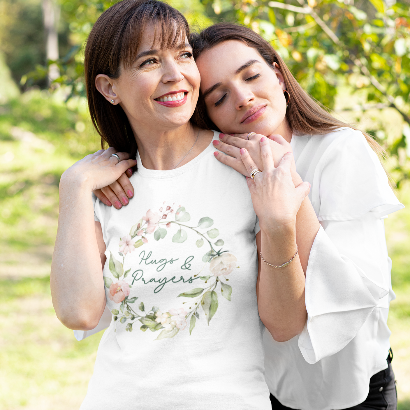Smiling woman wearing a Hugs and Prayers Tshirt receiving a hug from her daughter.