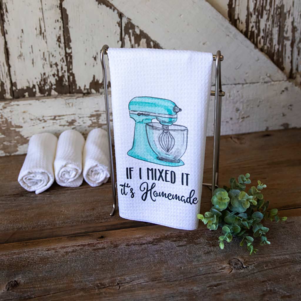 If I mixed it it's Homemade dish towel with a blue stand mixer image on it, hanging in front of a white barn door with several rolled towel in the background and a sprig of succulent in the foreground.