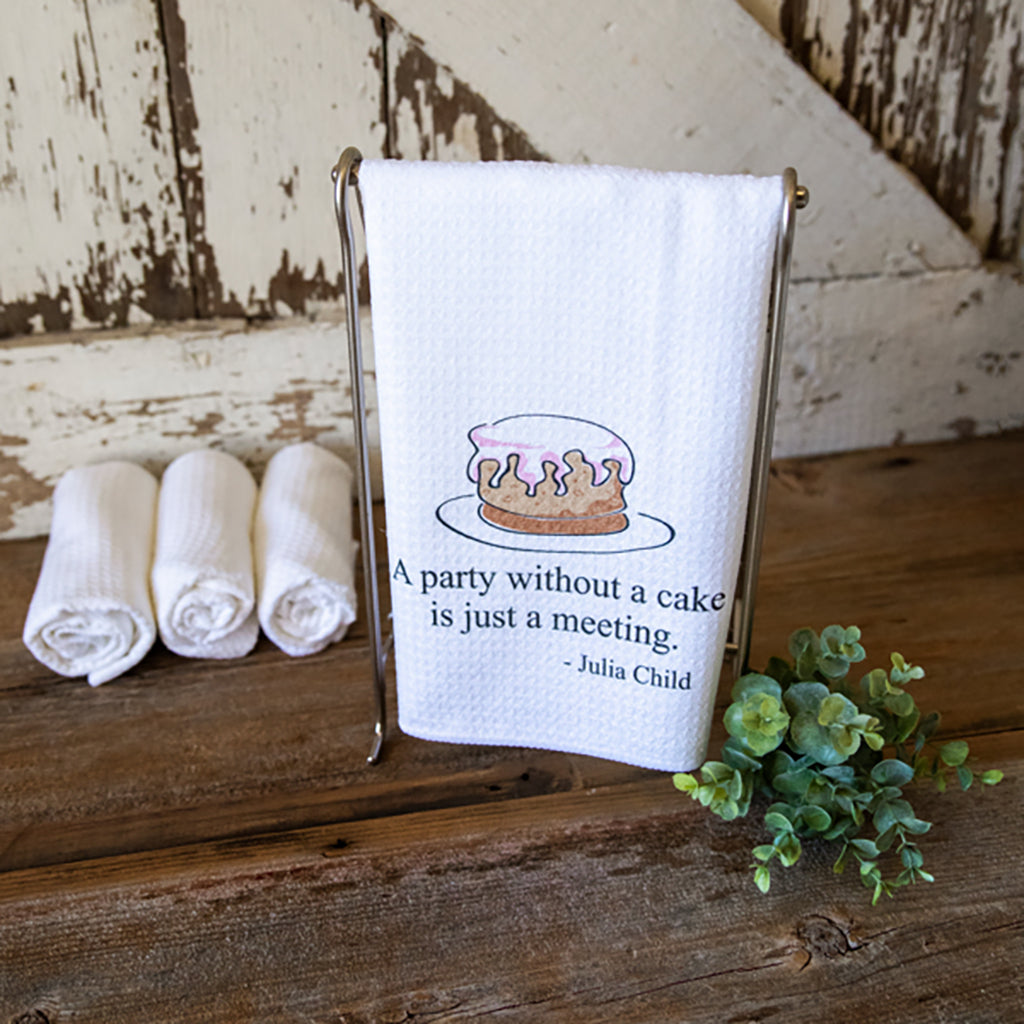 A dish towel with a cute cartoony cake image and the words, "A party without a cake is just a meeting.  -Julia Child"
