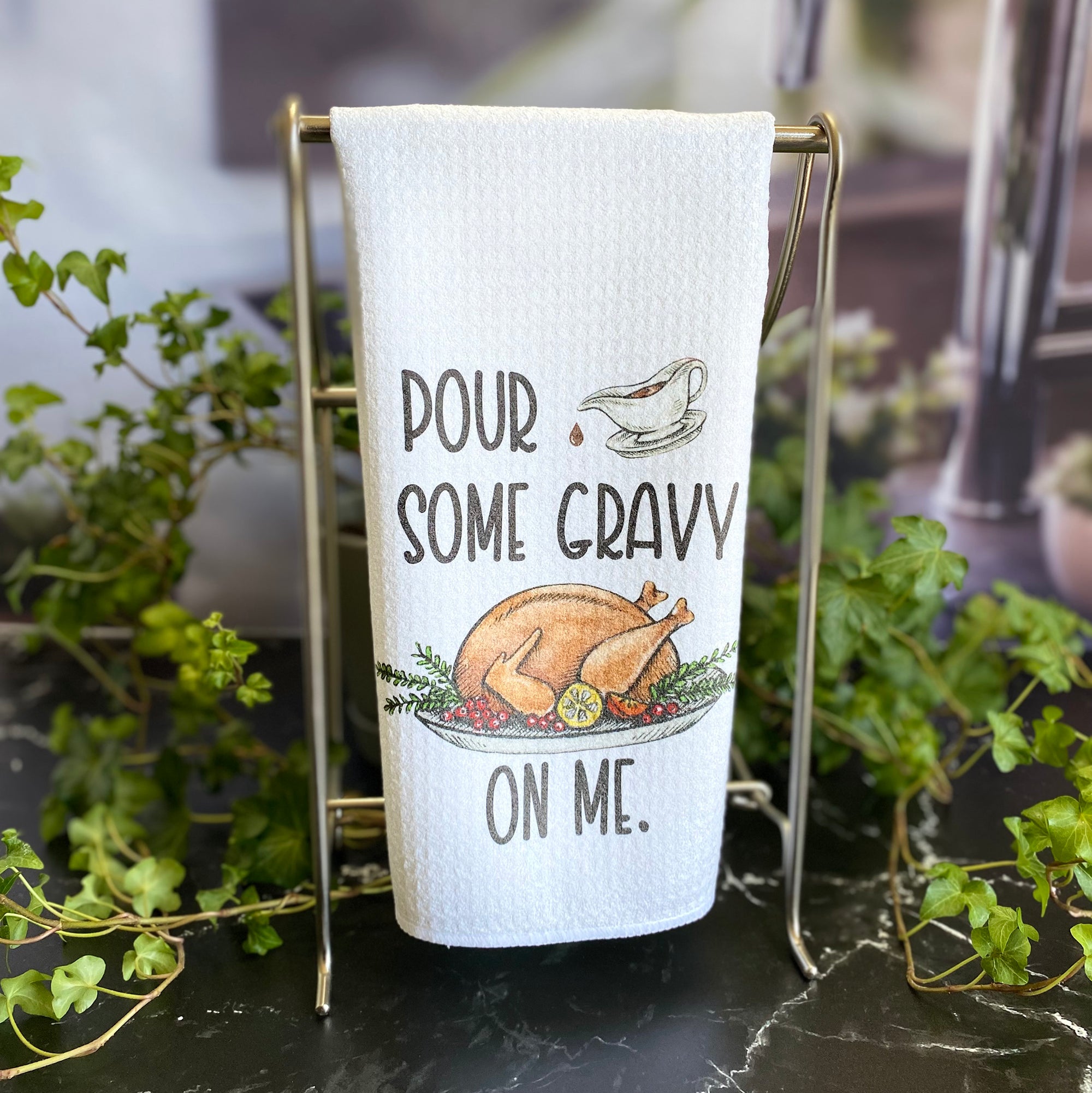 A white dishtowel  with a hand drawn image of a turkey on a platter with garnishes and a small gravy boat, pouring a drip of gravy onto the words, "Pour some gravy on me." in all caps