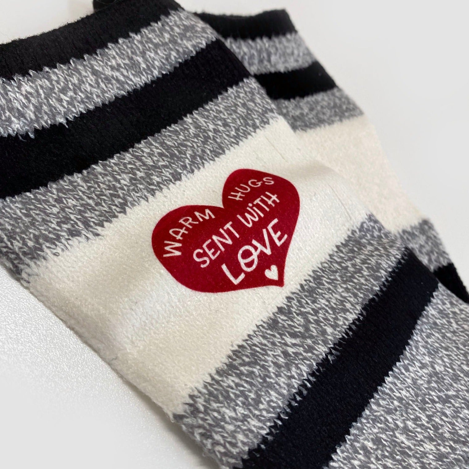 Gray and Black Socks with a wide white Stripe with a red heart that says, "Warm Hugs sent with Love" with a small white heart at the bottom.